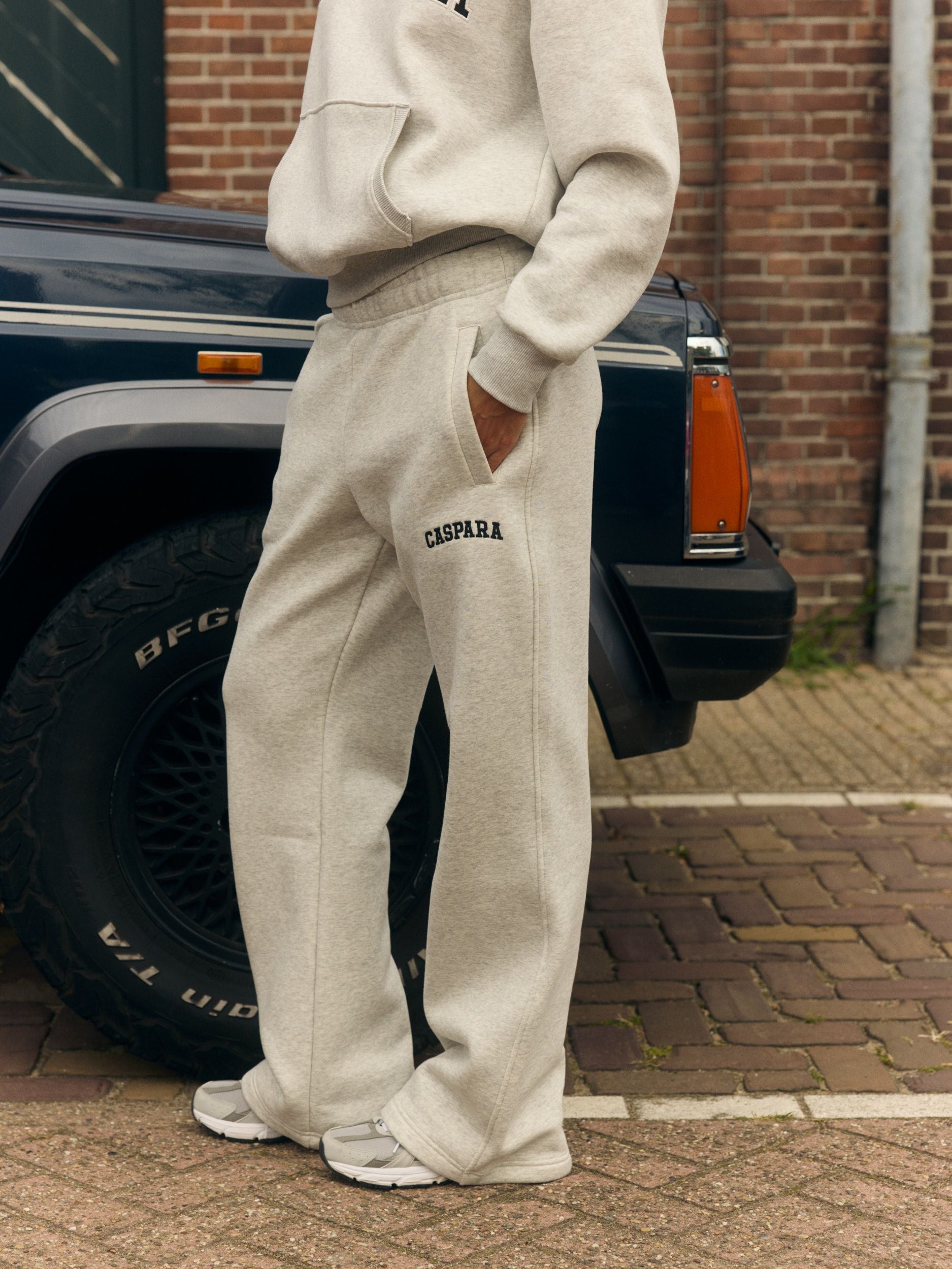 Woman wearing grey melange straight-leg sweatpants and matching hoodie beside a vintage car.
